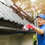 man cleaning gutter on a ladder