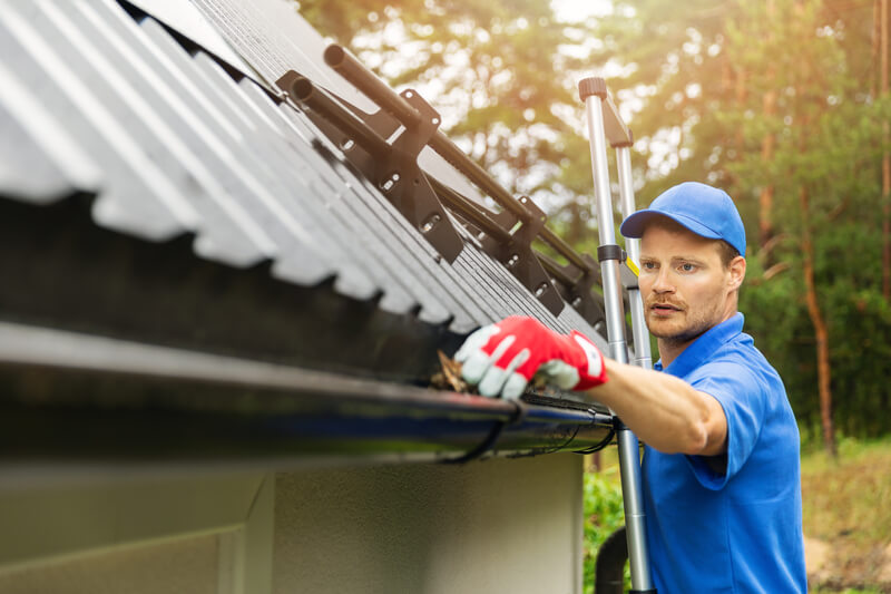 man cleaning gutter on a ladder