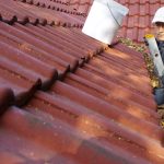 Man cleans the gutter on a roof.